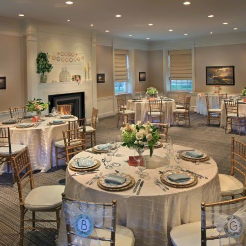 The image shows an elegantly set dining room with round tables, chairs, and floral centerpieces, creating a cozy and inviting atmosphere.