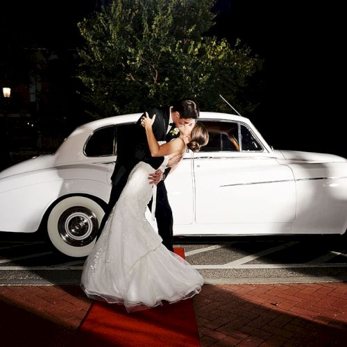 A couple in formal attire shares a romantic dance pose in front of a classic white car at night.