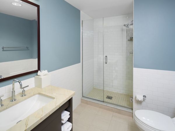 A clean bathroom with a shower, sink, mirror, and toilet. The design features blue walls and a glass-enclosed shower area.