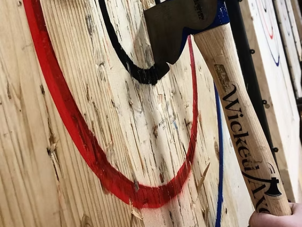 A hand hammers a metal tip into a wooden board marked with red and black spray lines, a blue cord nearby, hammering action paused.