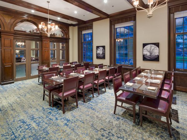 The image shows an elegant dining room with wooden decor, tables set for a meal, and large windows, creating a cozy, upscale ambiance.