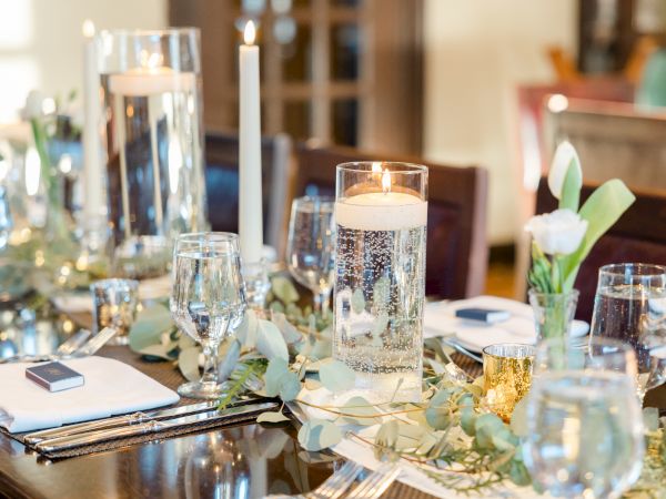 A beautifully set dining table features candles, glassware, flowers, and elegant decor, creating a sophisticated and inviting atmosphere.