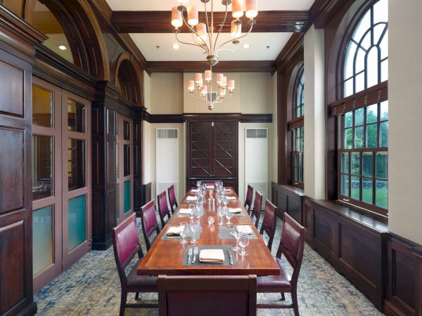An elegant dining room with a long wooden table, set for a meal, surrounded by chairs, and lit by a chandelier.