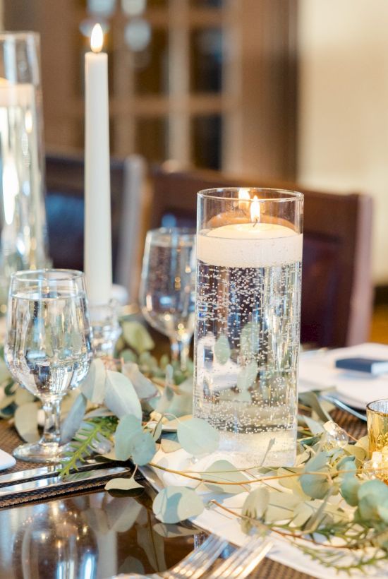 A beautifully set dining table features candles, glasses, napkins, and floral arrangements, creating an elegant and inviting atmosphere.