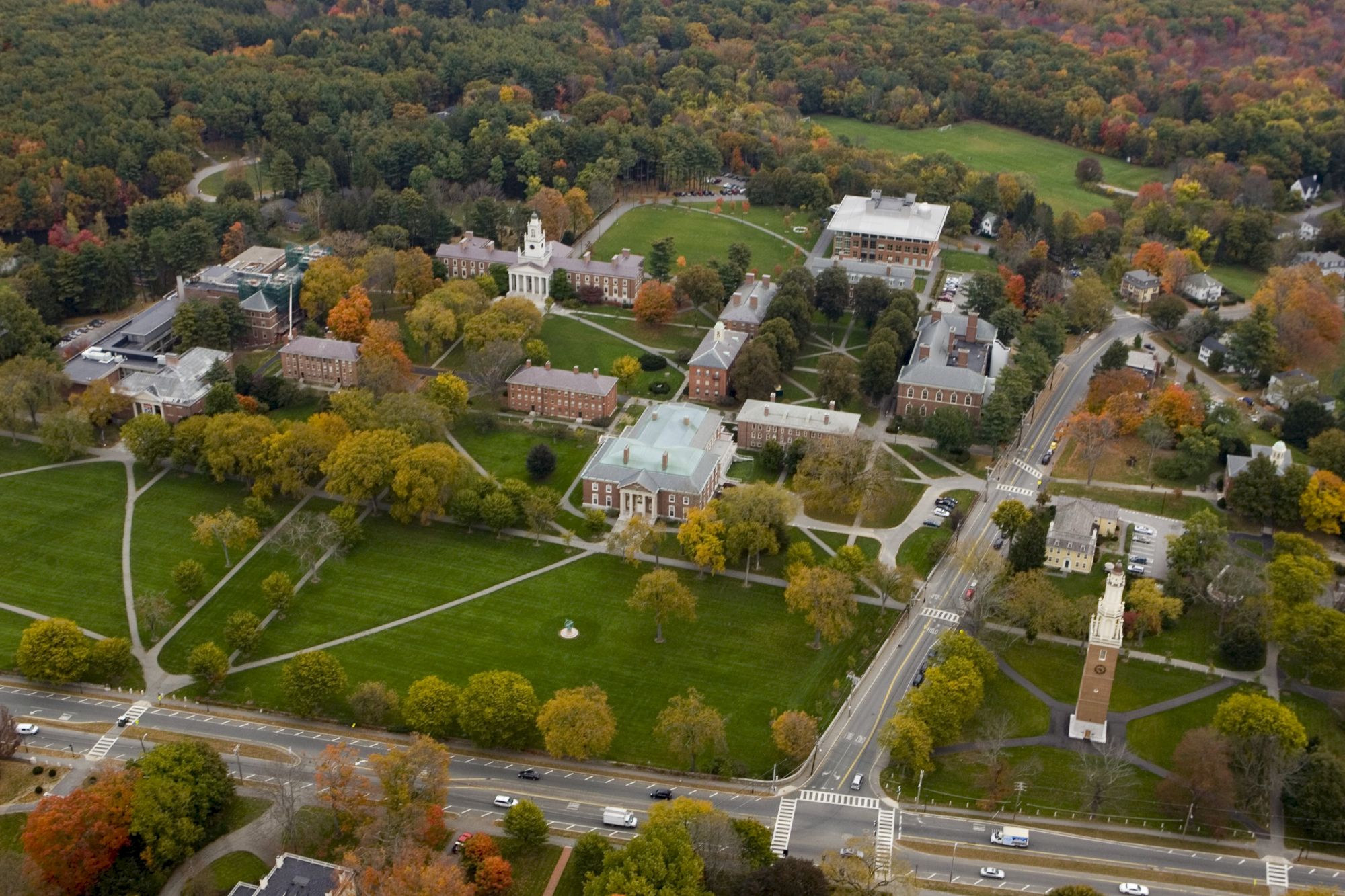 An aerial view of a campus with multiple buildings, green lawns, and surrounding trees in autumn colors, intersected by roads.