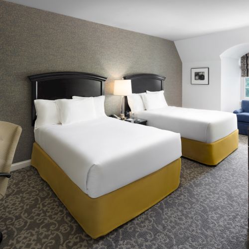 The image shows a hotel room with two beds, a desk with a chair, a TV, and a window with a view.