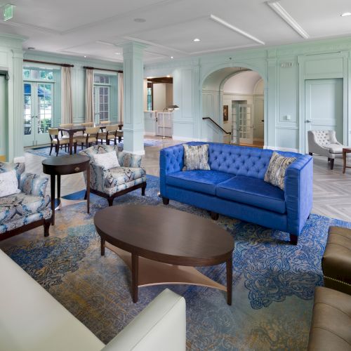 The image shows a spacious, modern lounge with sofas, armchairs, tables, and decorative accents, creating a comfortable seating area.