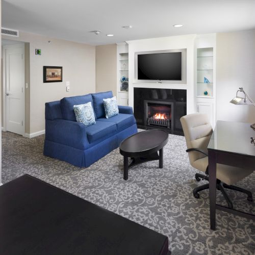 A cozy living room with a blue sofa, fireplace, TV, desk, and chair, creating a comfortable and inviting atmosphere.